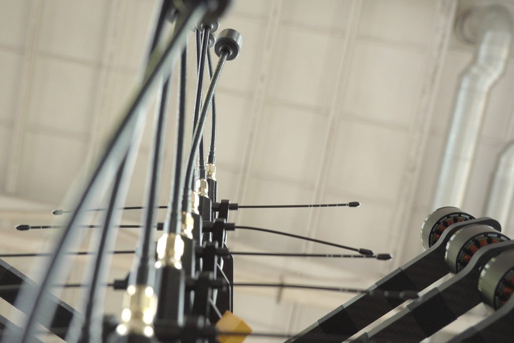 Close-up of an FPV racing drone from below — antennas, motor pods, wiring
